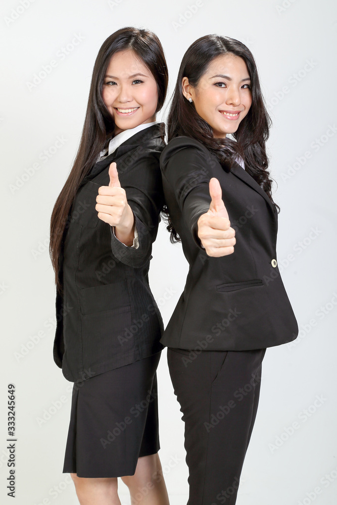 Two young asian malaysian business office woman stand smile thumbs up hand sign on white background Two young asian malaysian business office woman stand smile thumbs up hand sign on white background