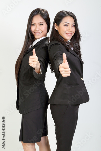 Two young asian malaysian business office woman stand smile thumbs up hand sign on white background