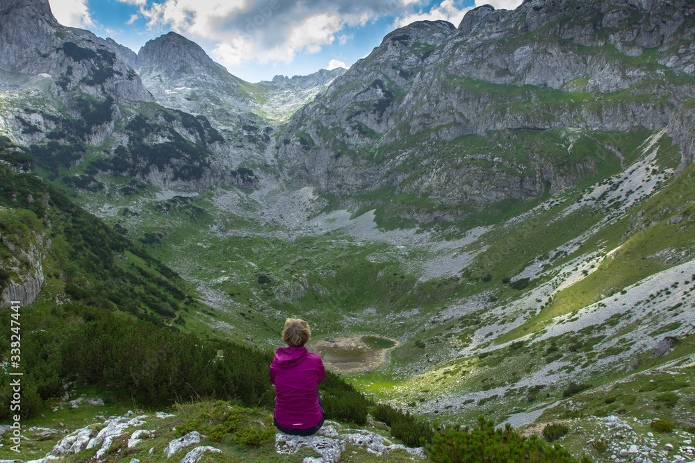 Girl enjoying a view of wild nature and mountains. Green summer mountains. Girl in a pink jacket. Female traveler. Hiking day