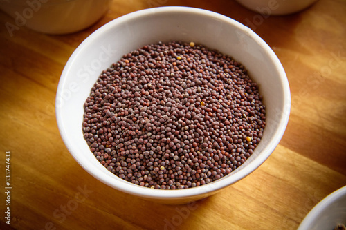 brown mustard seeds in white bowl on wooden background