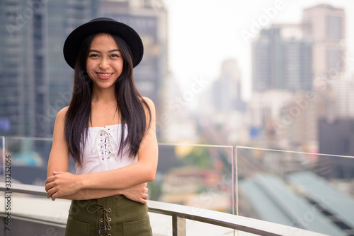 Happy young beautiful Asian tourist woman against view of the city