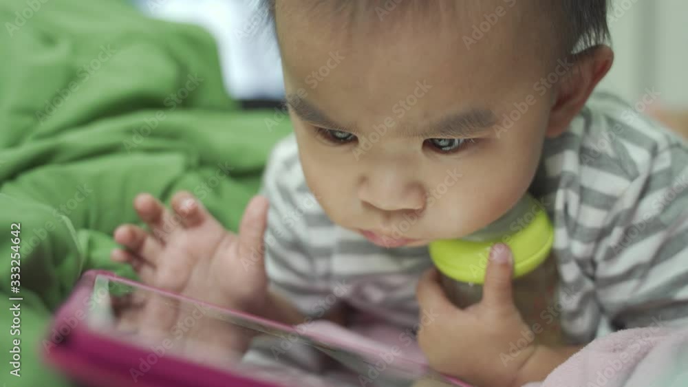 Baby boy with a bottle of milk Look at the tablet Then slide the tablet to play on the bed Baby boy with a bottle of milk Look at the tablet Then slide the tablet to play on the bed