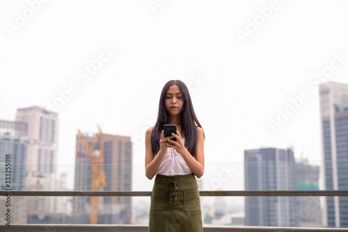 Young beautiful Asian tourist woman using phone against view of the city