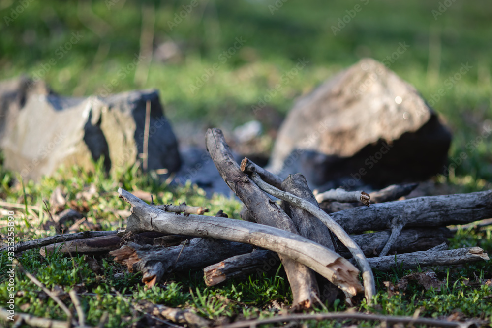 Firewood for a fire piled in a pile against a background of stones and green grass. With blurry background. Firewood for a fire piled in a pile against a background of stones and green grass. With blurry background.