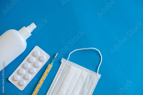 A set of medical disposable mask, antiseptic, pills and a mercury thermometer on a blue background. Medical hygiene and virus protection concept. Top view. Copy, empty space for text