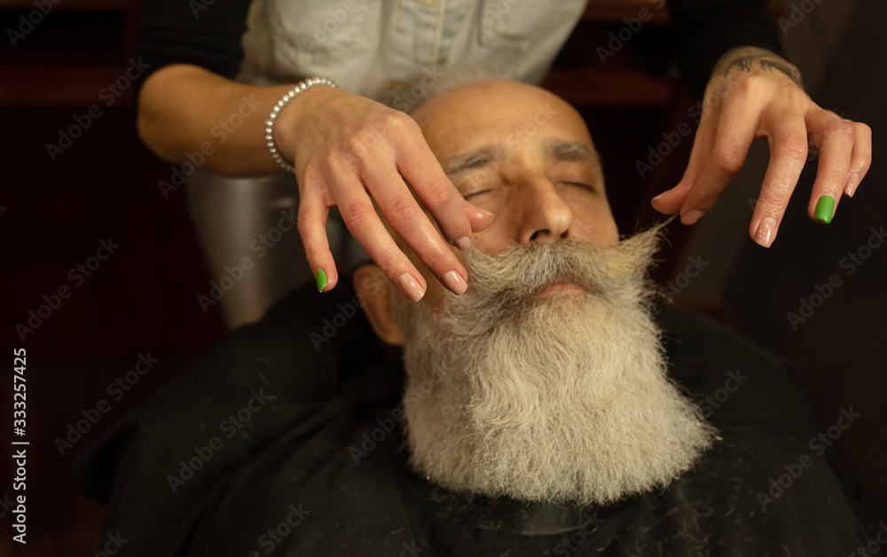 Handsome senior man getting styling and trimming of his beard in the barbershop. Handsome senior man getting styling and trimming of his beard in the barbershop.