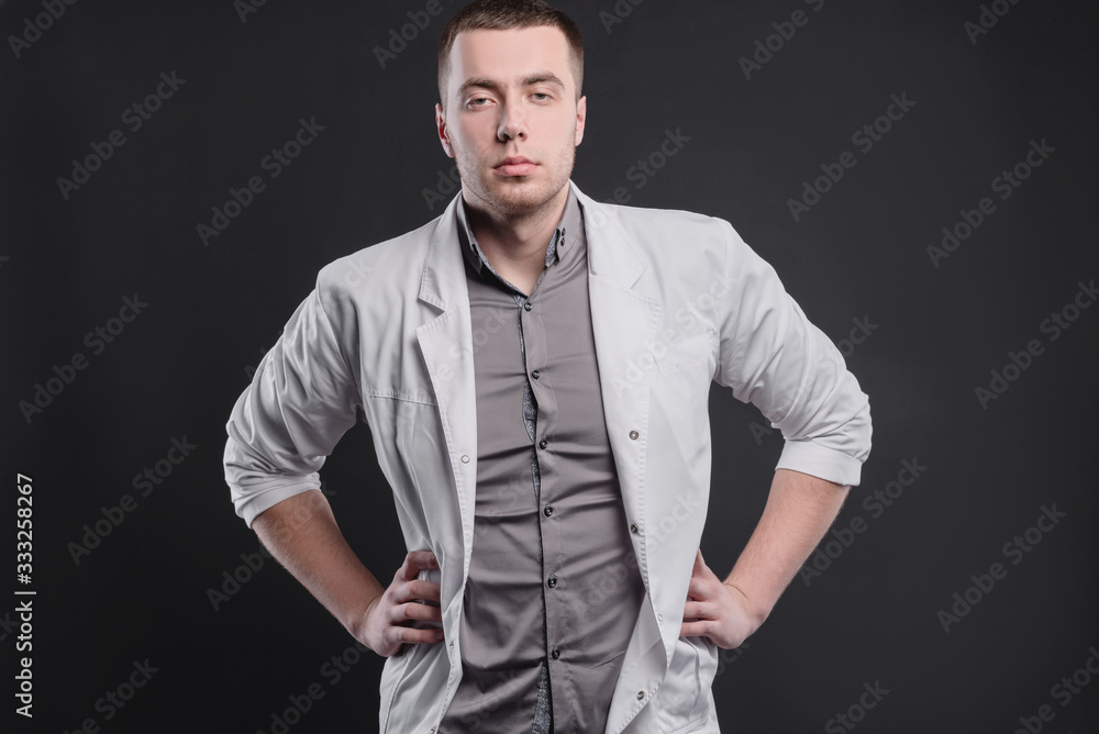 Young, pretty man in a medical coat on a gray background. The concept of medical education and medical activity
