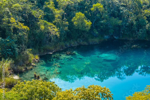 View of the Cenote of Candelaria in Huehuetenango  Guatemala  on a sunny day where you can see the turquoise color of the water and the reflection of the trees in the water.