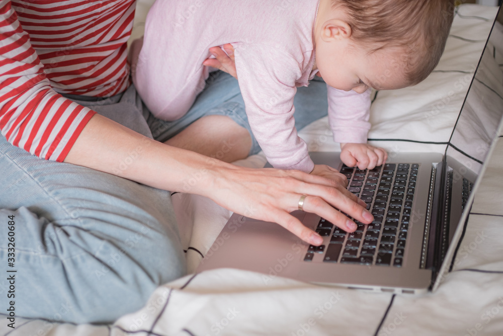 Naklejka premium Mother working on laptop at home together with infant baby. Distance work, education. work from home, working mother.