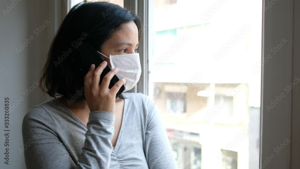 portrait of young woman infected with corona virus with face mask looking out of window while in quarantine with sad and worried expression due to self isolation portrait of young woman infected with corona virus with face mask looking out of window while in quarantine with sad and worried expression due to self isolation