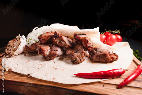 Appetizing fried meat lies on a wooden tray, among the seasonings. Studio photography of food in the cooking industry, dark background