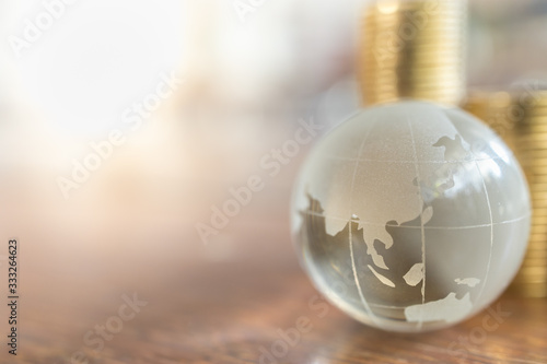 Fototapeta Naklejka Na Ścianę i Meble -  Global Business and Financial, Economic and palnning Concept. Close up of clear crystal world mini ball with stack of gold coins on wooden table and copy space.