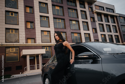 Stylish young girl stands near the car in a black dress. Business fashion and style © Andrii