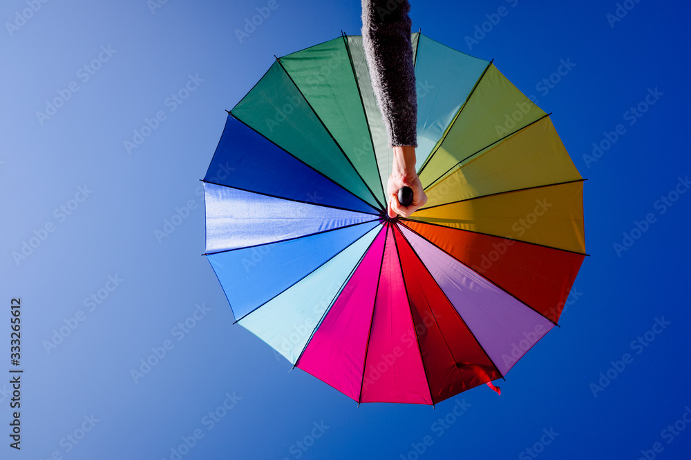Woman holds an umbrella of vibrant colors with the background of a clear blue sky.