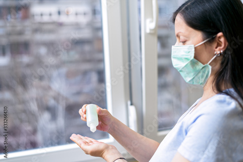 Young woman wearing protective medical mask while applying hand sanitizer