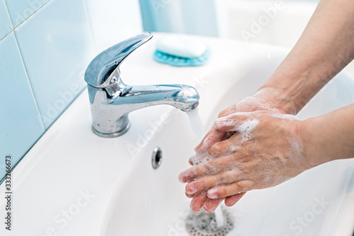 Woman washing hands with soap under the water tap