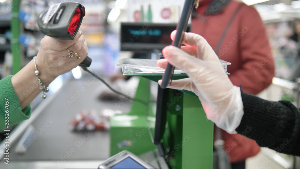 A woman at the checkout in a supermarket gives a customer a card with a laser from her smartphone. Paying in the supermarket in protective gloves so as not to get coronavirus A woman at the checkout in a supermarket gives a customer a card with a laser from her smartphone. Paying in the supermarket in protective gloves so as not to get coronavirus