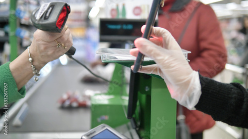 A woman at the checkout in a supermarket gives a customer a card with a laser from her smartphone. Paying in the supermarket in protective gloves so as not to get coronavirus