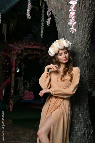 spring girl in a beige dress and a flower wreath on her head among the trees