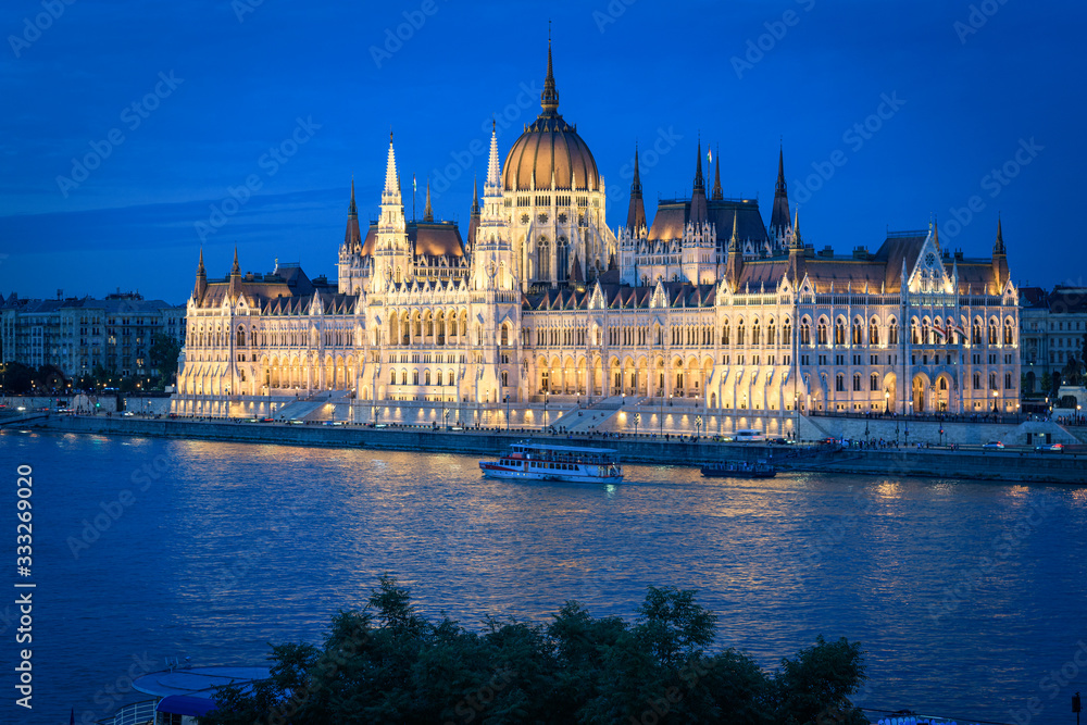 Fototapeta premium The Budapest Parliament at blue hour. Boats passing by on Danube river, Hungary 2019