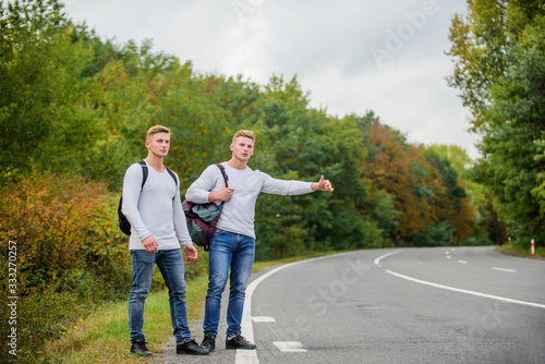 type of adventure. On the road. Enjoying summer hike. Looking for transport. twins walking along road. stop car with thumb up gesture. hitchhiking and stopping car with thumbs up gesture