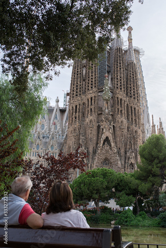 couple looking at La Sagrada Familia, tourists looking at La Sagrada Familia, people opposite La Sagrada Familia, Tourists in Barcelona near Gaudi Temple, an elderly couple of tourists in Barcelona