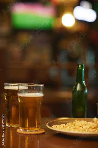 Close-up of two glasses of beer with plate of snacks on the wooden table in the bar