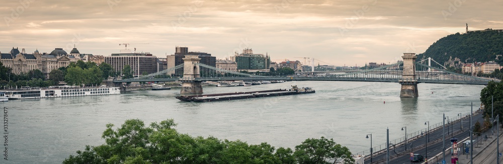 Budapest Chain Bridge at dawn, panoramic view. A barge is passing on the Danube river, Hungary