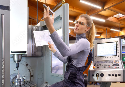 A young woman works as a computerized  numerical control technician. She is seen at her workplace wearing a blue overall. 
