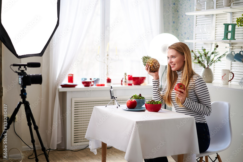 Food blogger cooking fresh vegan salad of fruits in kitchen studio, filming tutorial on camera for video channel. Female influencer holds apple, pineapple and talks about healthy eating. Fructorianism Food blogger cooking fresh vegan salad of fruits in kitchen studio, filming tutorial on camera for video channel. Female influencer holds apple, pineapple and talks about healthy eating. Fructorianism