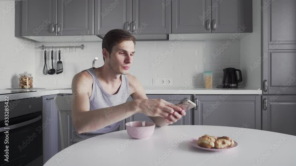 Young man eating soup and using phone at the kitchen Young man eating soup and using phone at the kitchen