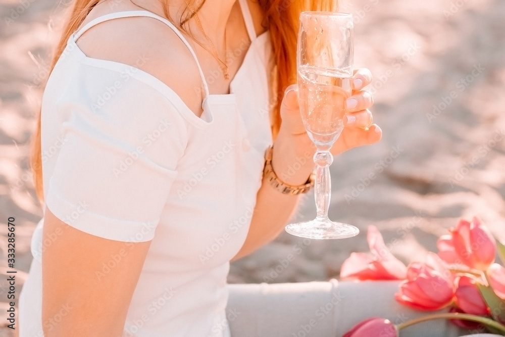 Obraz premium .beautiful girl stands on a sandy beach with a bottle of champagne. romantic walk at dawn with the rays of the sun..
