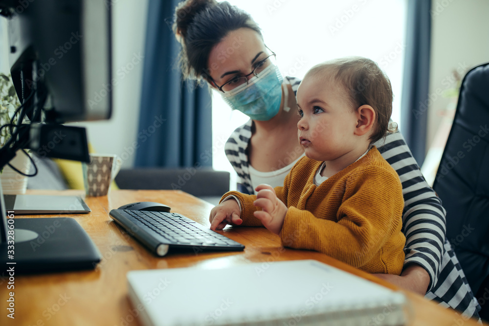 Young mother working with her baby on computer at her home office. Young mother working with her baby on computer at her home office.