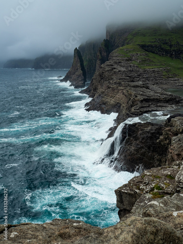 Faroe Islands, Vagar, Bøsdalafossur waterfalls. View on the waterfall and cliffs towering above the ocean. Harsh landscape.