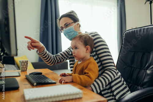 Young mother working with her baby on computer at her home office. photo