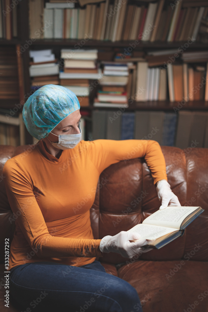 Obraz premium Woman with protective antiviral mask sitting at home in isolation / quarantine and reading book.