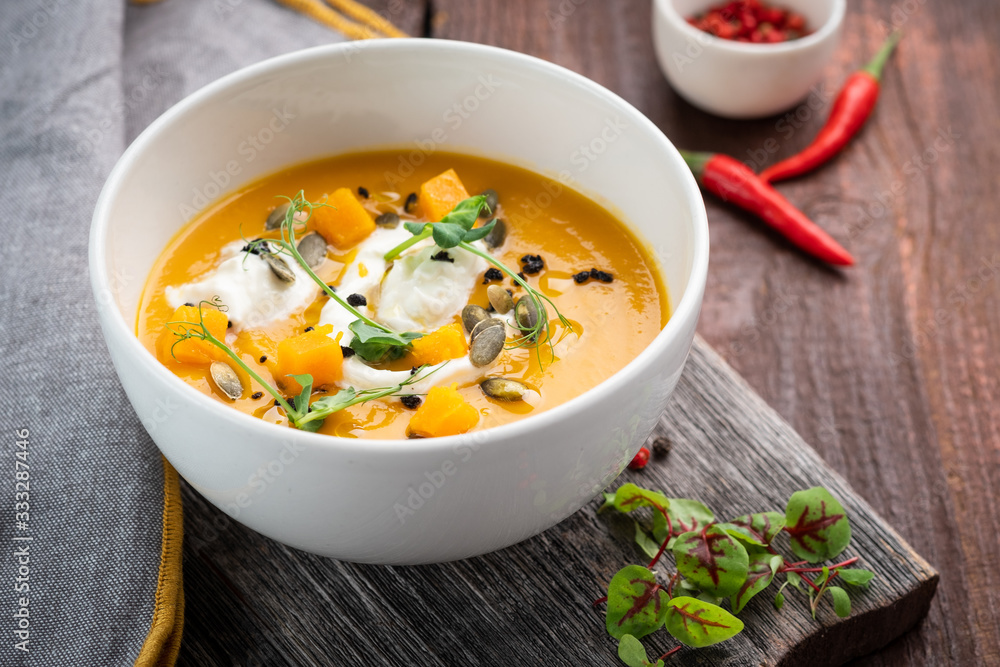 Bright colored pumpkin cream Soup with seeds and herbs in a white bowl on a wooden background, rustic style Bright colored pumpkin cream Soup with seeds and herbs in a white bowl on a wooden background, rustic style