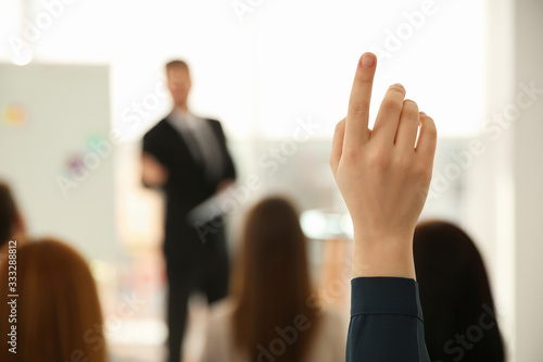 Young woman raising hand to ask question at business training indoors, closeup photo