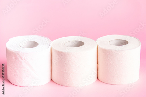 Three rolls of white toilet paper close-up on a pink background 