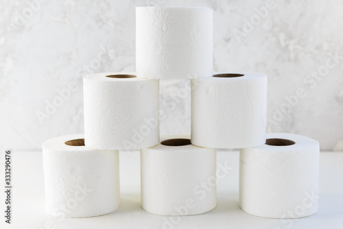 Rolls of white toilet paper in the form of a pyramid on a white table.
