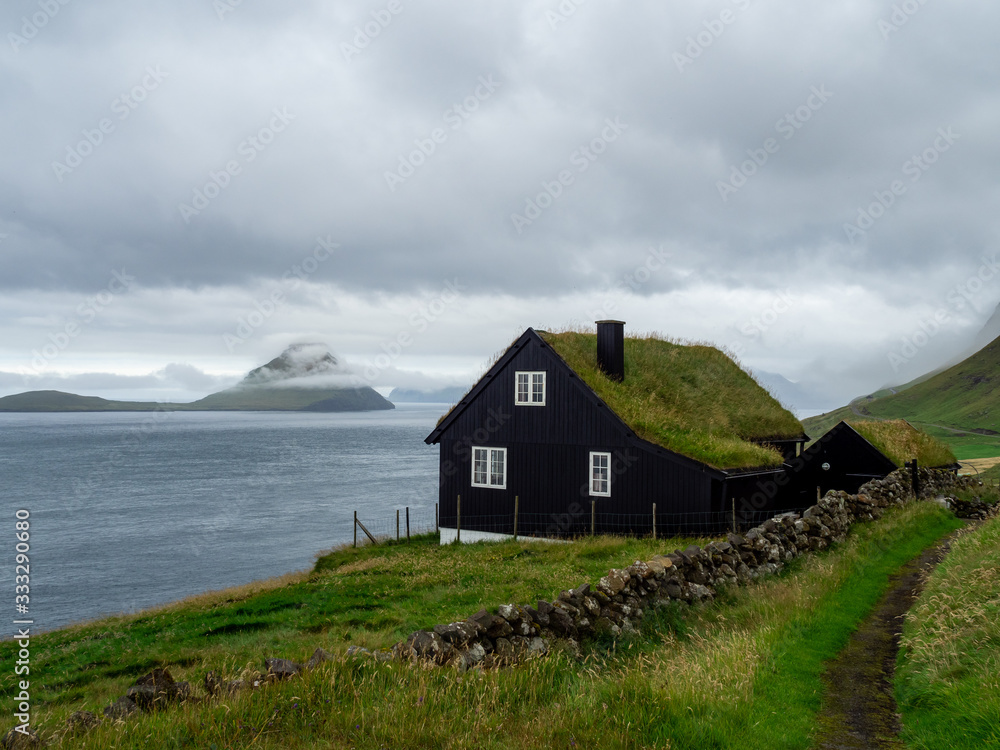 Faroe Islands. House with grass roof on the slope of hill. Hazy landscape. Cloudy weather. Faroe Islands. House with grass roof on the slope of hill. Hazy landscape. Cloudy weather.