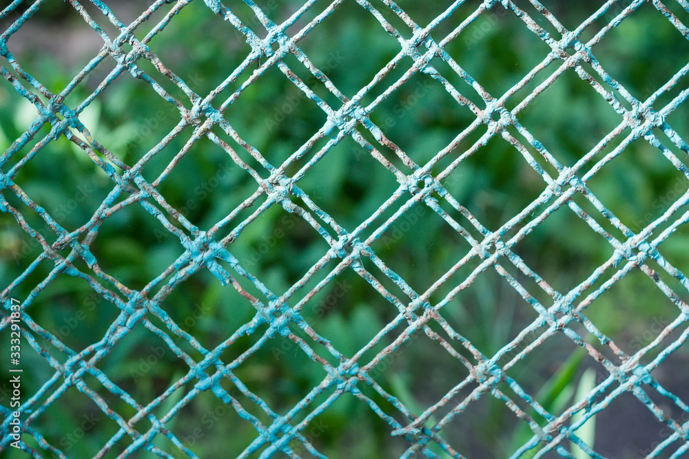 Fototapeta premium Light green old weathered painted mesh fence detail (selected focus)