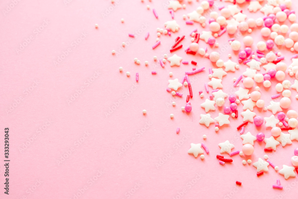 Festive frame made of colorful pastel sprinkles on a pink background, copy space on top. Sprinkle sugar with balls and stars, decoration for cake and bakery products.