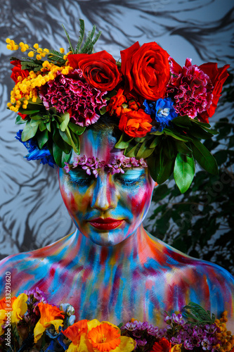 Portrait of a girl whose face is painted with colored paints in a wreath of flowers. In Frida Kahlo's footsteps