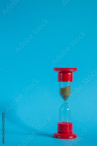Red glass hourglass close-up against a blue background with copy space.