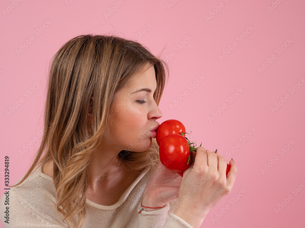 Adult female with closed eyes kissing bunch of fresh tomatoes while being on diet against pink background Adult female with closed eyes kissing bunch of fresh tomatoes while being on diet against pink background
