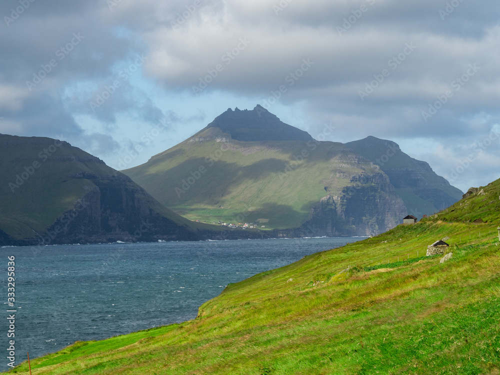 Faroe Islands. View over the bay and green grass slopes of hills. Hazy landscape.