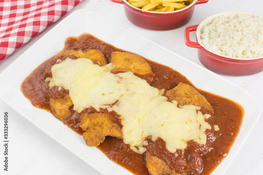Veal parmigiana in a white platter with rice in and french fries in white background seen from above