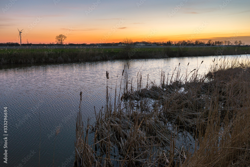 Dutch landscape with reed along the bank of a small river. Twilight colors above the horizon. Dutch landscape with reed along the bank of a small river. Twilight colors above the horizon.