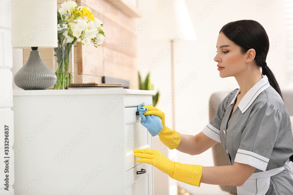 Young chambermaid wiping dust from furniture in hotel room Young chambermaid wiping dust from furniture in hotel room
